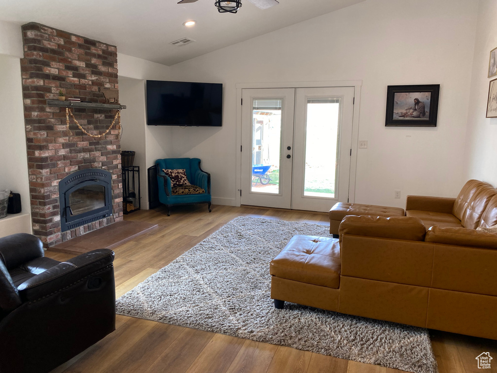 Living room featuring a fireplace, lofted ceiling, brick wall, wood-type flooring, and french doors