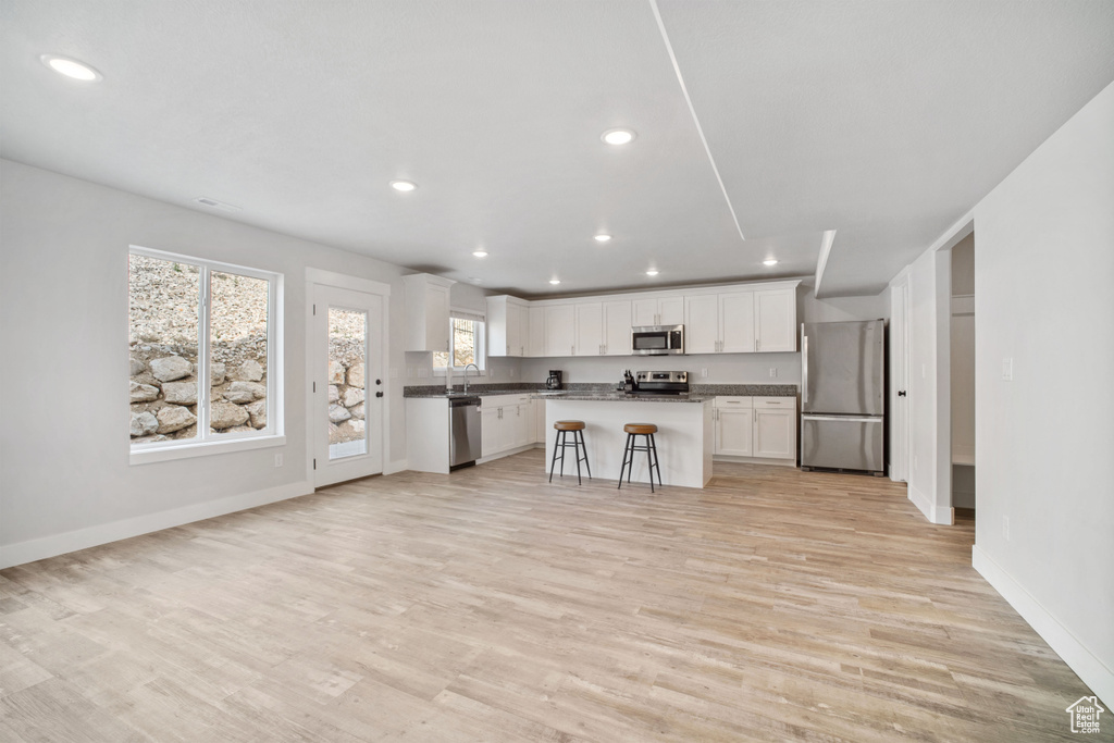 Kitchen with light hardwood / wood-style flooring, white cabinetry, appliances with stainless steel finishes, a breakfast bar area, and a kitchen island