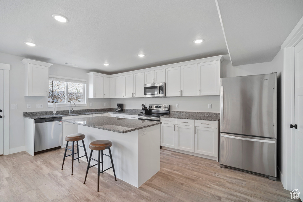 Kitchen featuring a kitchen island, white cabinetry, a breakfast bar area, stainless steel appliances, and light hardwood / wood-style flooring