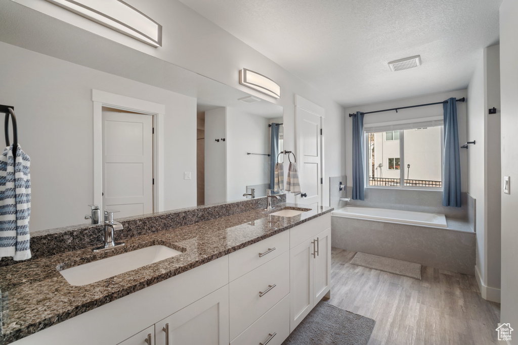 Bathroom with vanity with extensive cabinet space, a bathtub, wood-type flooring, a textured ceiling, and dual sinks
