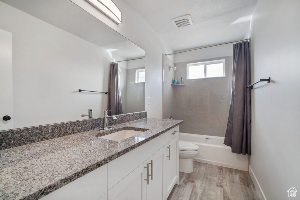 Full bathroom featuring hardwood / wood-style floors, vanity, shower / bathtub combination with curtain, and toilet