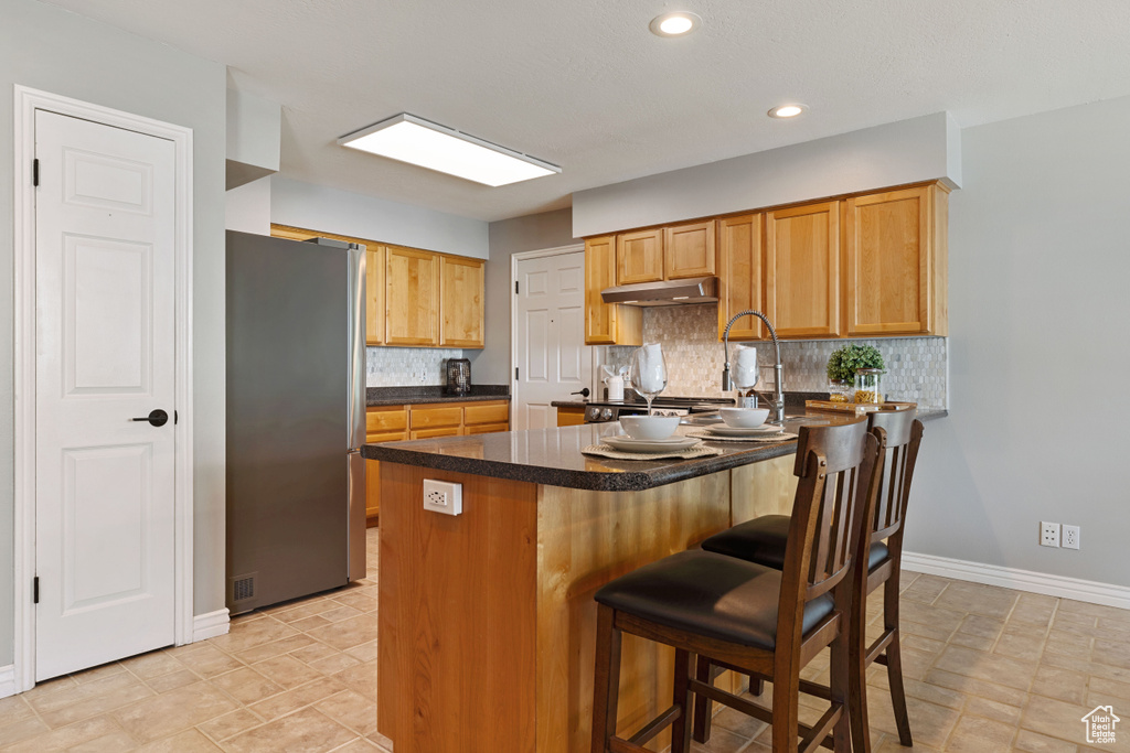 Kitchen featuring stainless steel refrigerator, kitchen peninsula, light tile floors, and backsplash