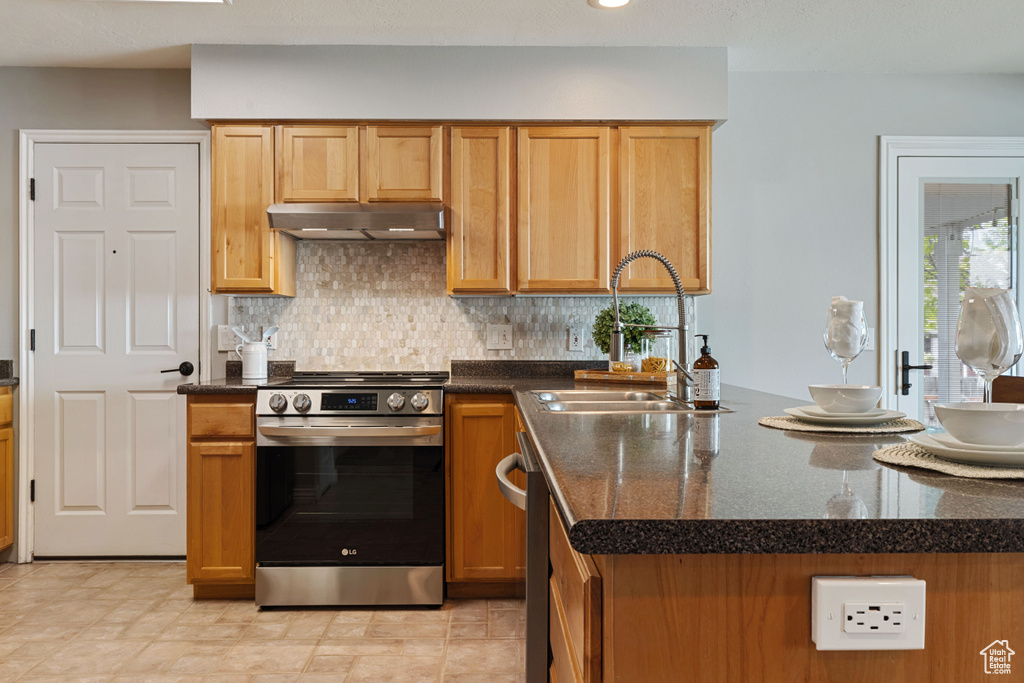 Kitchen featuring stainless steel range oven, backsplash, light tile floors, sink, and dark stone countertops