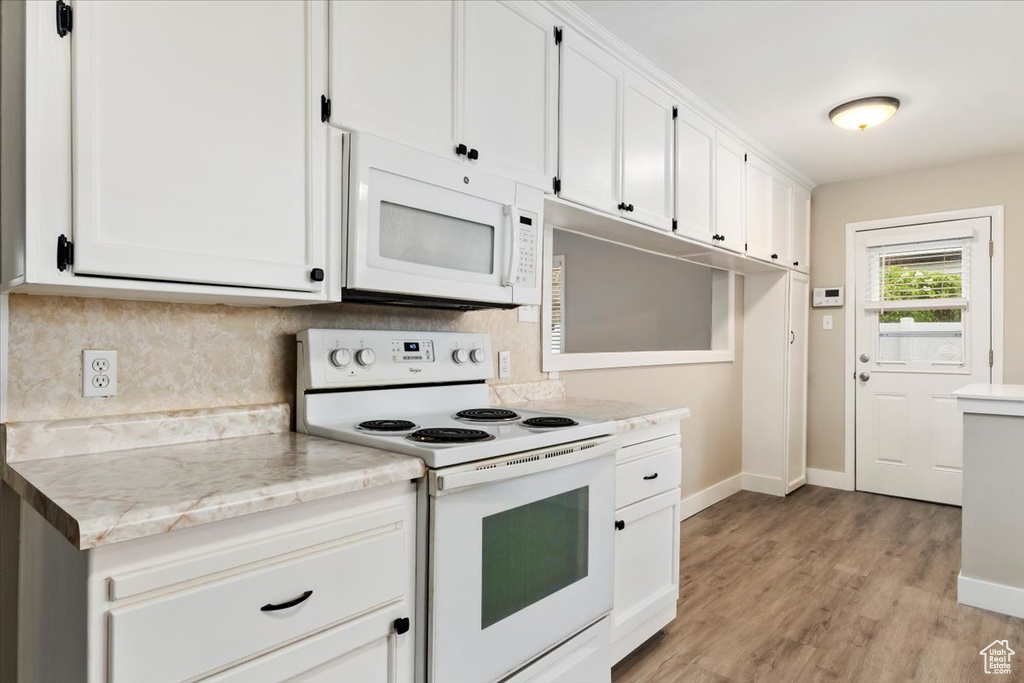 Kitchen featuring backsplash, light hardwood / wood-style flooring, white appliances, light stone counters, and white cabinets