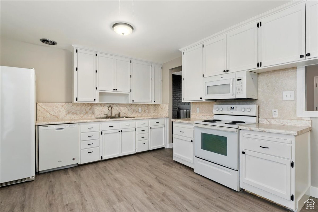 Kitchen featuring white cabinets, sink, light hardwood / wood-style floors, white appliances, and tasteful backsplash