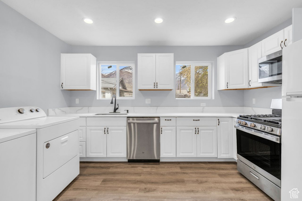 Kitchen with a wealth of natural light, stainless steel appliances, white cabinets, and hardwood / wood-style floors