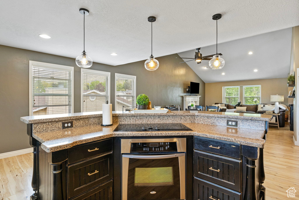 Kitchen featuring hanging light fixtures, vaulted ceiling, stainless steel oven, and light hardwood / wood-style floors