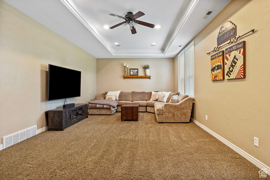 Living room with ornamental molding, ceiling fan, a raised ceiling, and carpet floors