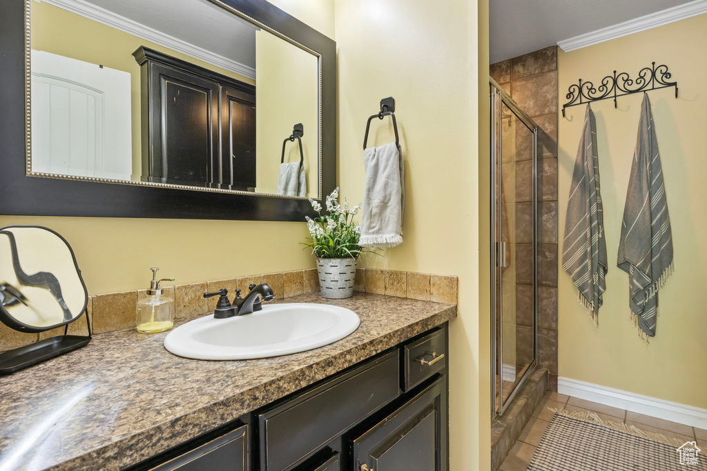 Bathroom with tile flooring, large vanity, a shower with shower door, and ornamental molding