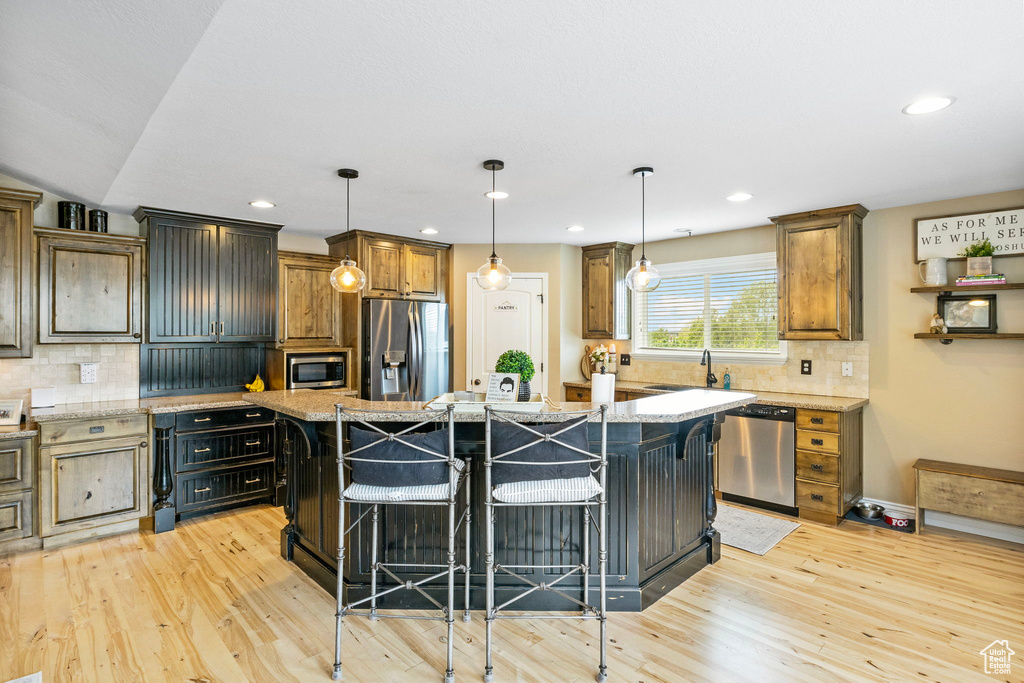 Kitchen featuring light stone countertops, appliances with stainless steel finishes, light hardwood / wood-style flooring, a kitchen island, and tasteful backsplash