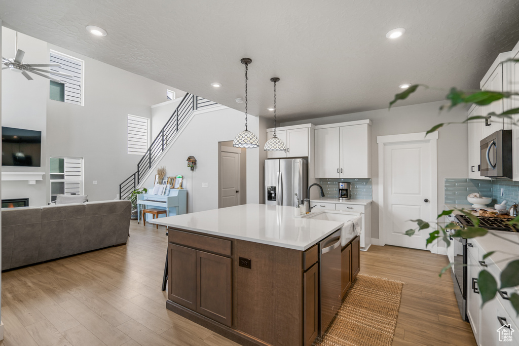 Kitchen with backsplash, light hardwood / wood-style flooring, stainless steel appliances, and an island with sink