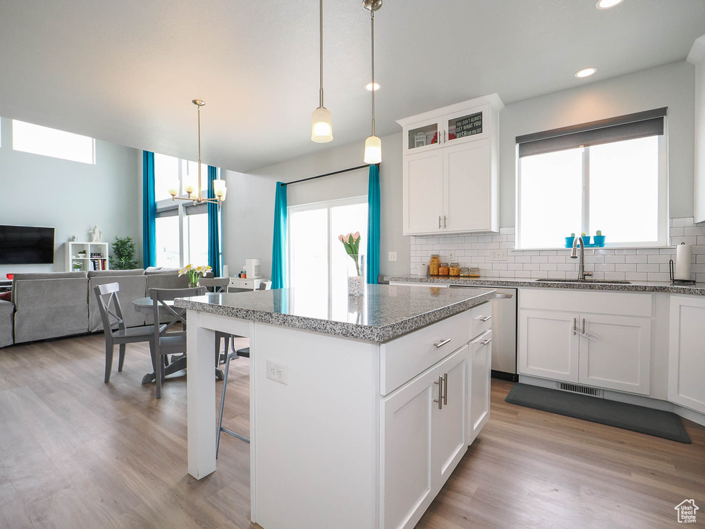 Kitchen featuring a kitchen island, sink, tasteful backsplash, decorative light fixtures, and light hardwood / wood-style flooring