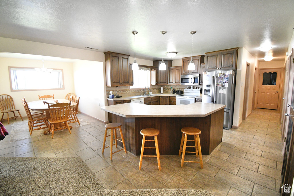 Kitchen with hanging light fixtures, appliances with stainless steel finishes, a kitchen island, and a wealth of natural light