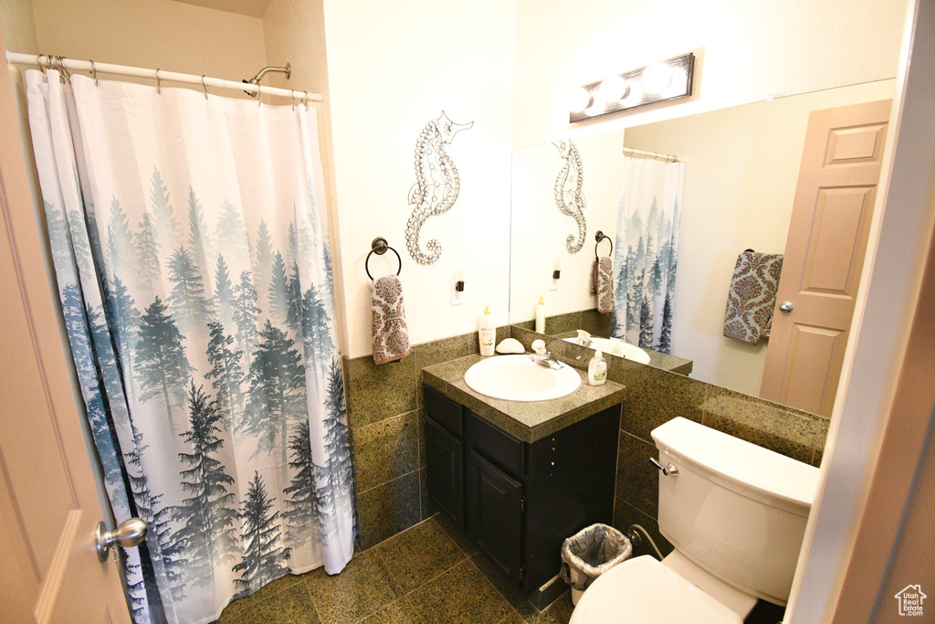 Bathroom featuring tile floors, tile walls, toilet, and large vanity