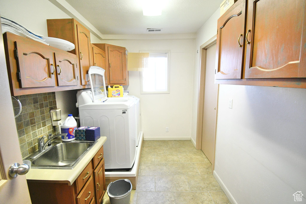 Washroom featuring cabinets, sink, light tile flooring, and washing machine and clothes dryer