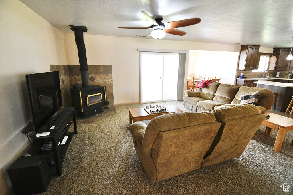 Living room featuring a wood stove, a healthy amount of sunlight, carpet flooring, and ceiling fan