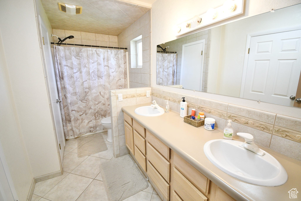 Bathroom featuring tile walls, tasteful backsplash, toilet, and dual vanity
