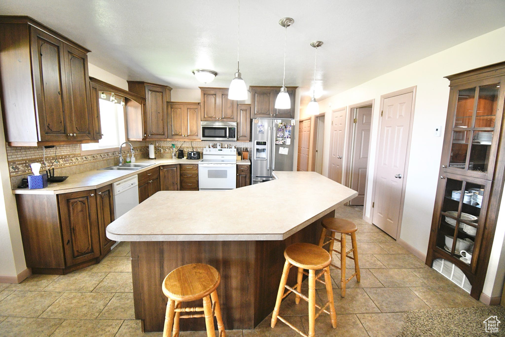 Kitchen featuring stainless steel appliances, light tile floors, sink, a kitchen island, and tasteful backsplash