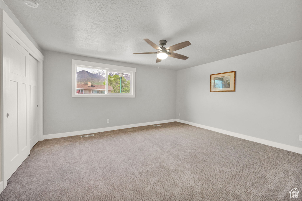 Unfurnished room with a textured ceiling, ceiling fan, and carpet