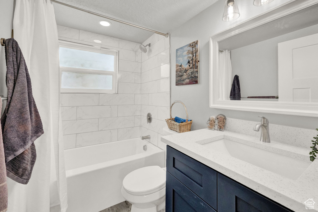 Full bathroom with a textured ceiling, vanity, toilet, and shower / tub combo