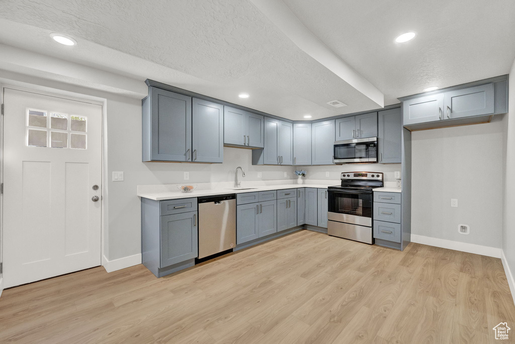Kitchen featuring appliances with stainless steel finishes, a textured ceiling, sink, and light wood-type flooring