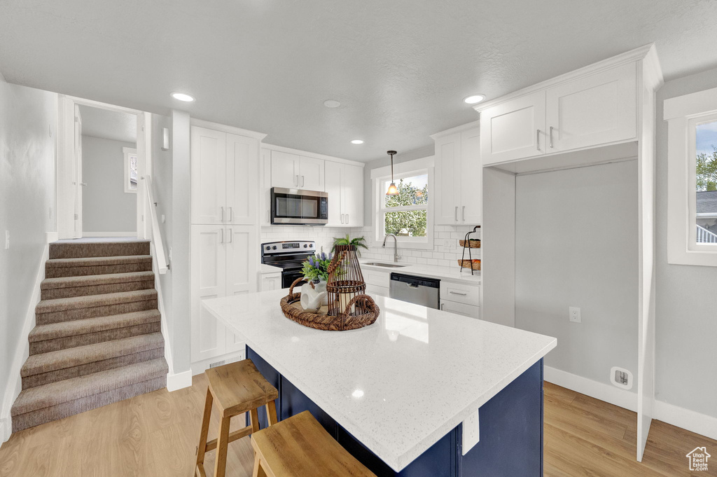 Kitchen featuring backsplash, stainless steel appliances, light hardwood / wood-style floors, white cabinetry, and a center island