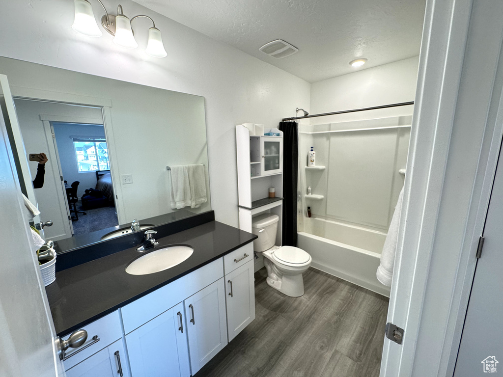 Full bathroom featuring large vanity, toilet, shower / tub combo with curtain, a textured ceiling, and hardwood / wood-style flooring