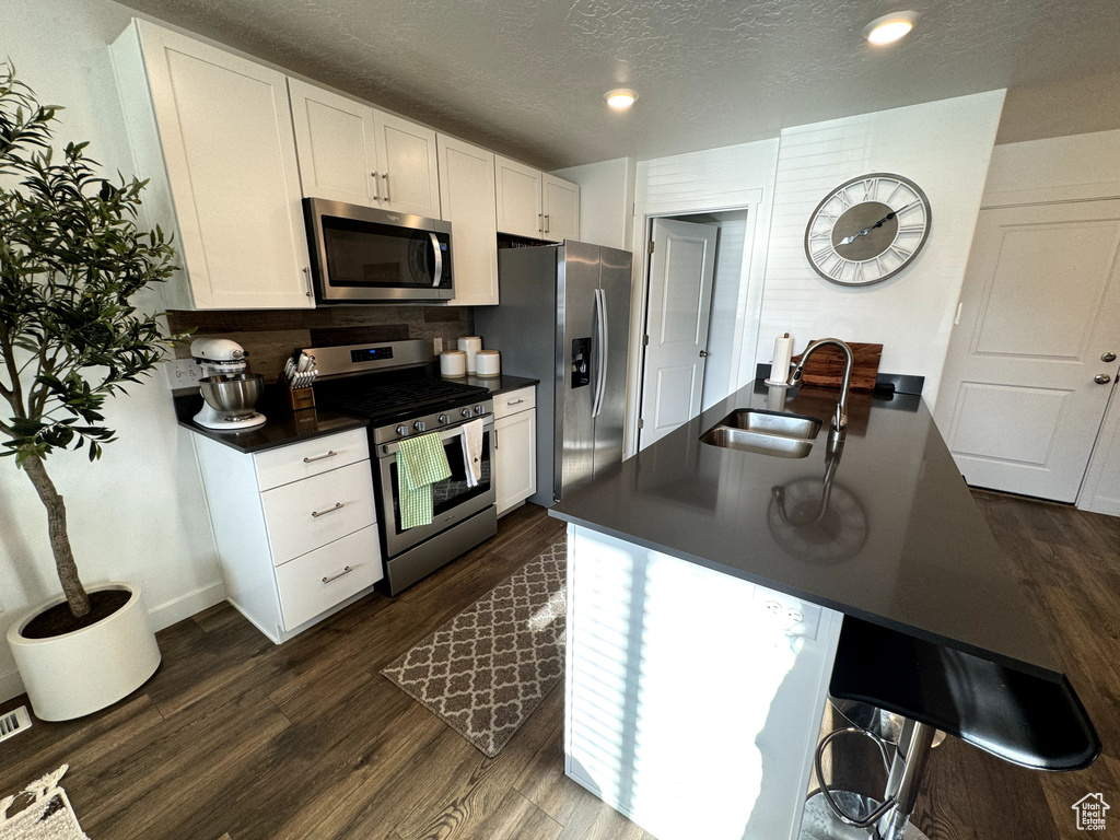 Kitchen with appliances with stainless steel finishes, dark wood-type flooring, white cabinets, and a kitchen bar