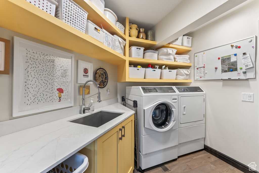 Laundry room featuring wood-type flooring, cabinets, sink, and washer and clothes dryer
