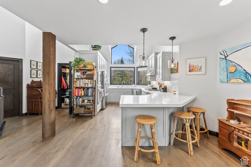 Kitchen with light hardwood / wood-style flooring, pendant lighting, kitchen peninsula, and a kitchen bar