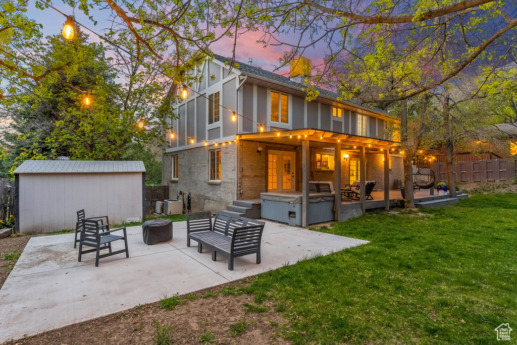 Back house at dusk featuring a patio, a lawn, a storage unit, and an outdoor living space with a fire pit