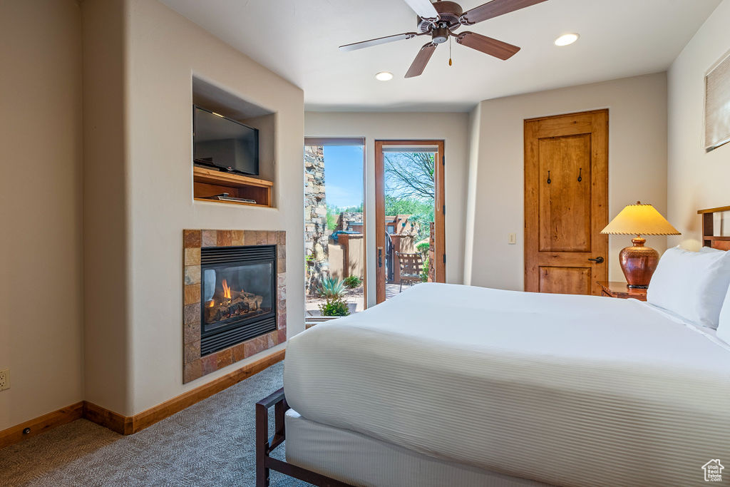 Carpeted bedroom with a fireplace, ceiling fan, and access to outside