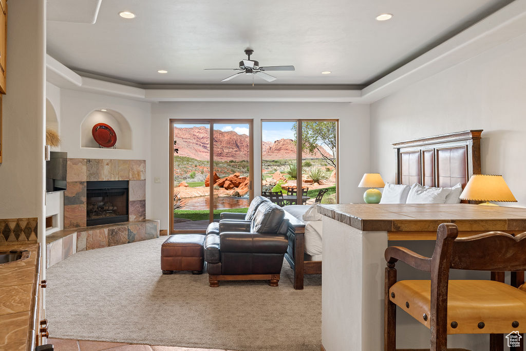 Carpeted living room featuring a raised ceiling, ceiling fan, and a tile fireplace