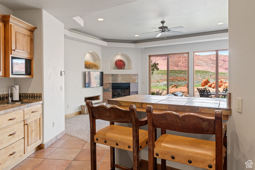 Dining space with a fireplace, a tray ceiling, light tile floors, sink, and ceiling fan