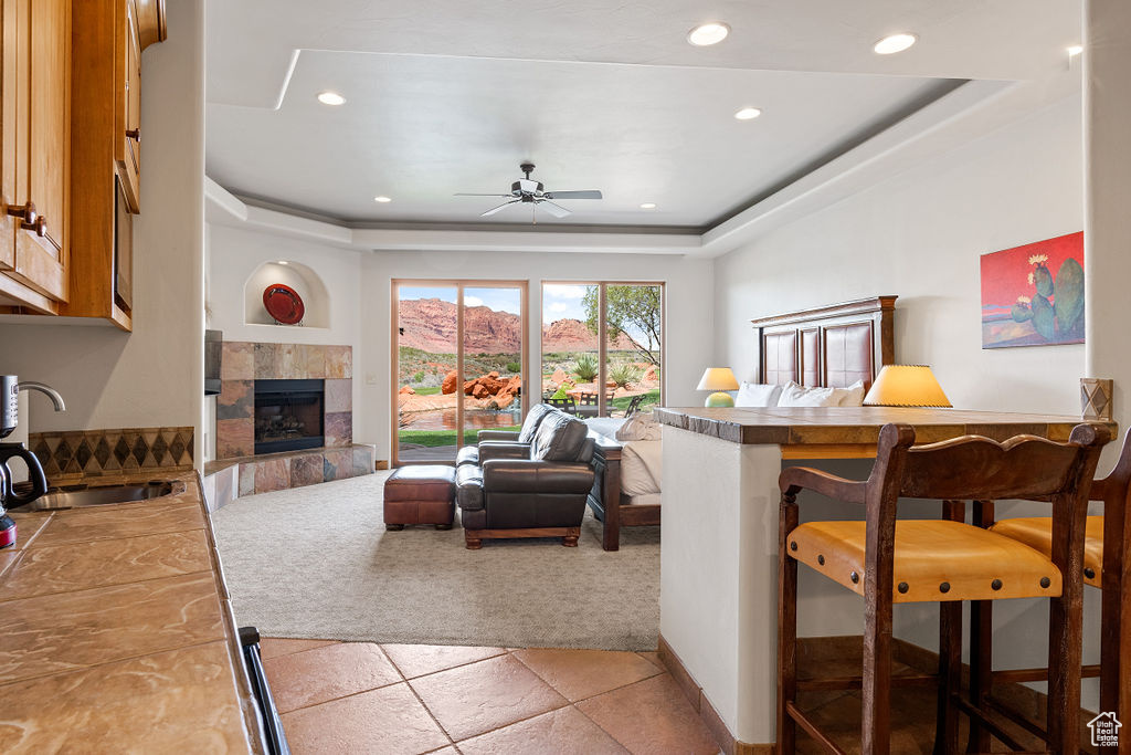 Living room featuring a fireplace, sink, ceiling fan, and a tray ceiling