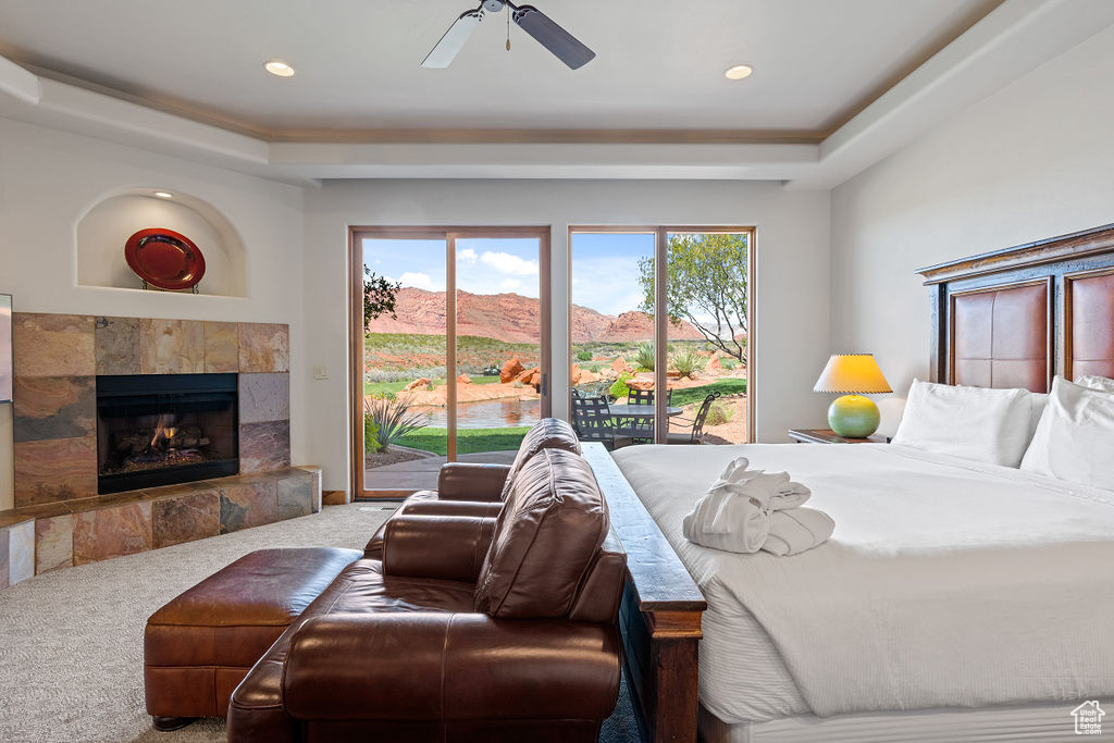 Carpeted bedroom with a tile fireplace, ceiling fan, a tray ceiling, and access to outside