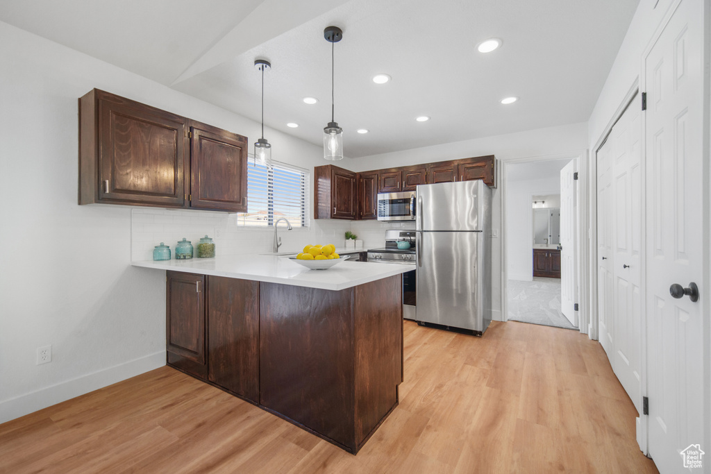 Kitchen featuring pendant lighting, light hardwood / wood-style flooring, kitchen peninsula, stainless steel appliances, and dark brown cabinetry