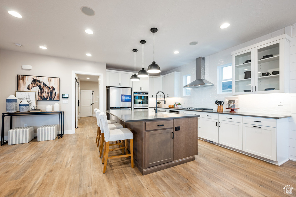 Kitchen featuring light hardwood / wood-style floors, appliances with stainless steel finishes, wall chimney range hood, and white cabinetry