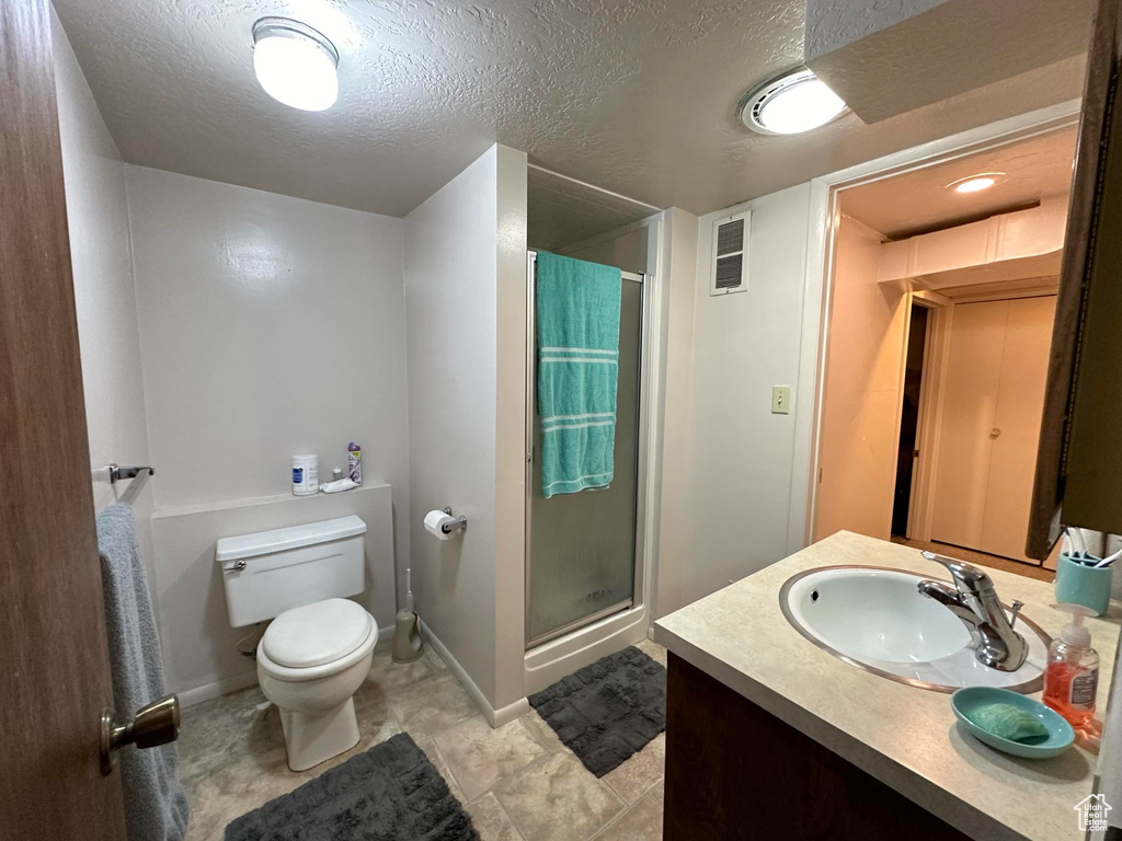 Bathroom featuring an enclosed shower, tile floors, vanity, toilet, and a textured ceiling