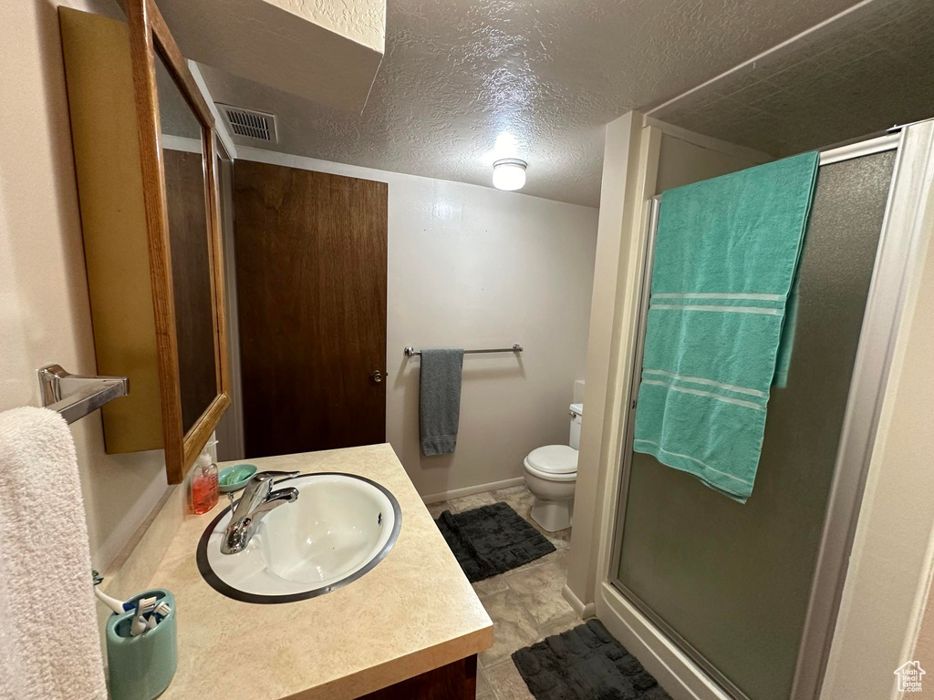 Bathroom featuring a textured ceiling, tile floors, toilet, vanity, and a shower with door