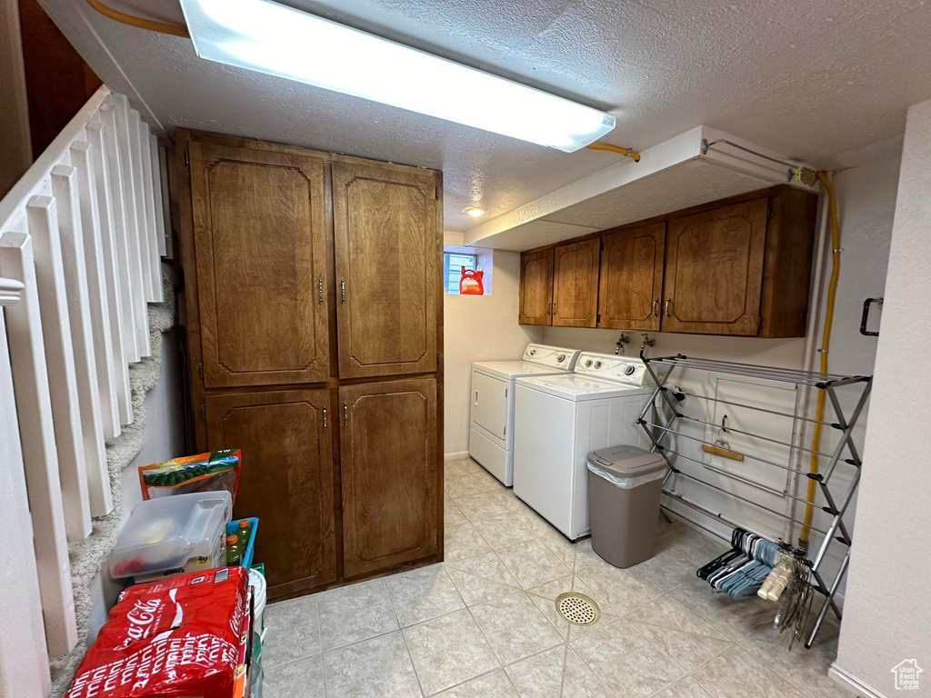 Clothes washing area featuring cabinets, light tile floors, a textured ceiling, washing machine and clothes dryer, and washer hookup