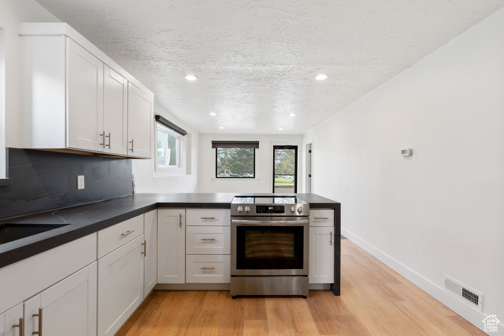 Kitchen featuring light hardwood / wood-style floors, tasteful backsplash, white cabinetry, and stainless steel electric stove