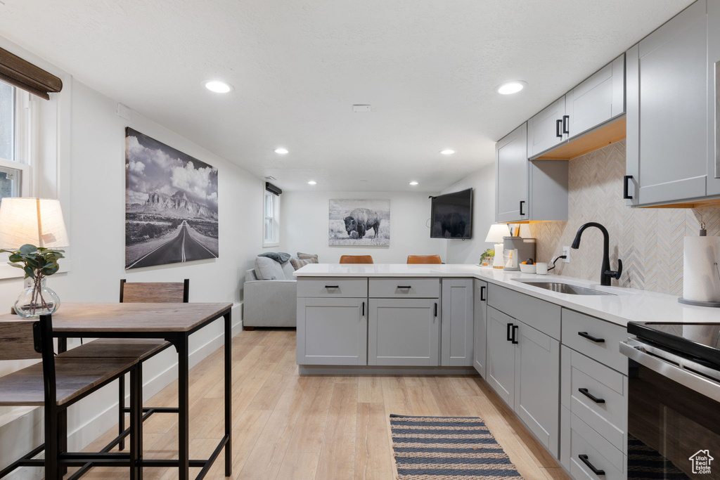 Kitchen with kitchen peninsula, gray cabinetry, light hardwood / wood-style flooring, tasteful backsplash, and sink