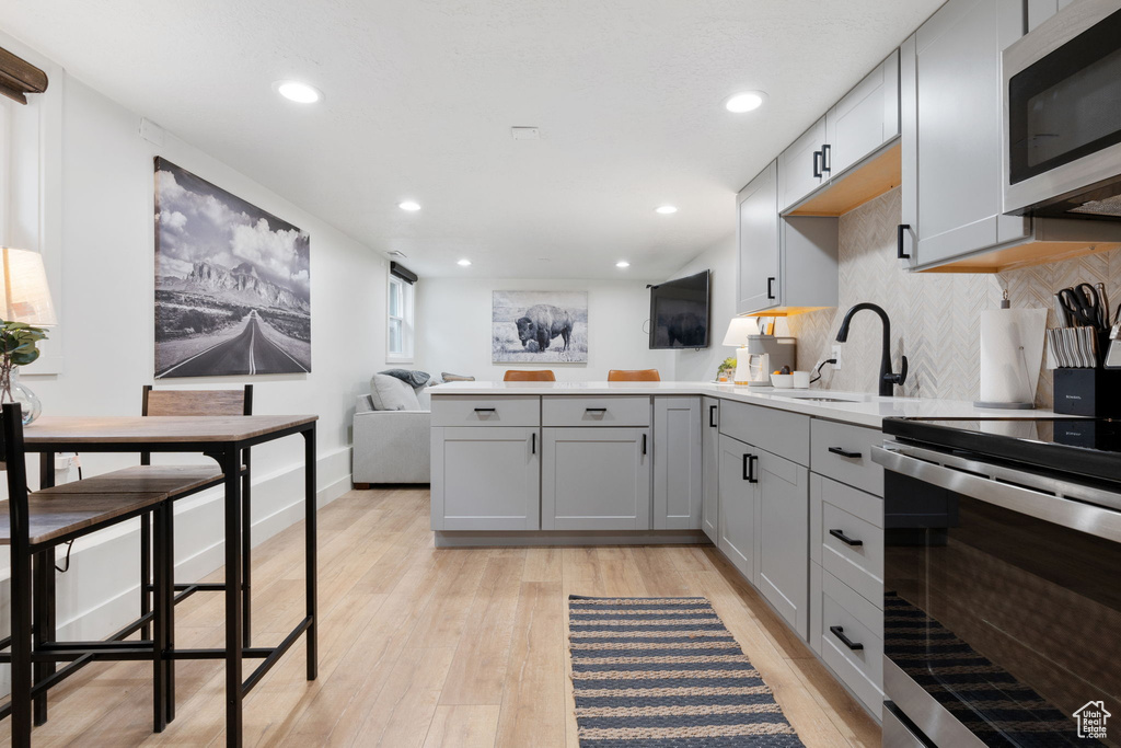 Kitchen with light hardwood / wood-style floors, backsplash, gray cabinets, stainless steel appliances, and kitchen peninsula