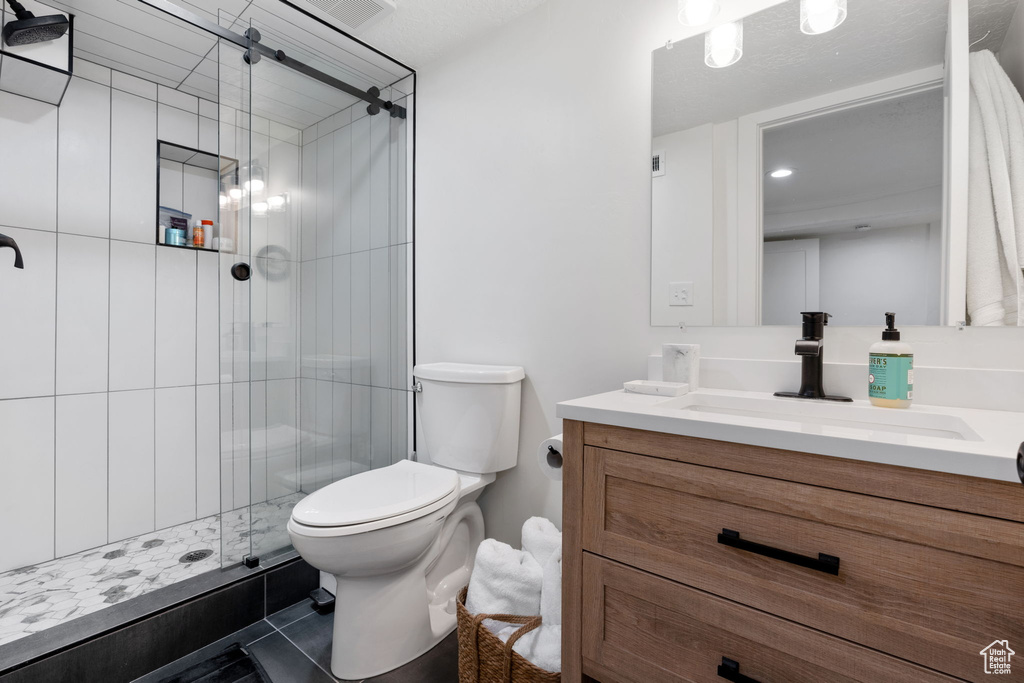 Bathroom with an enclosed shower, toilet, tile flooring, and vanity