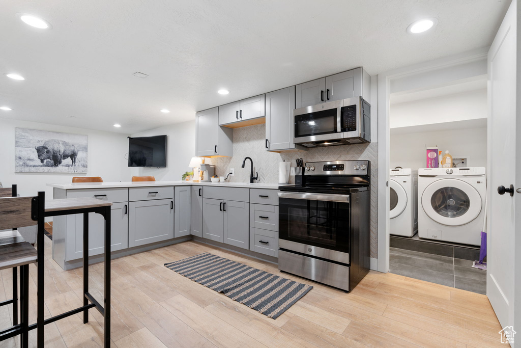 Kitchen with gray cabinetry, light hardwood / wood-style flooring, independent washer and dryer, appliances with stainless steel finishes, and tasteful backsplash