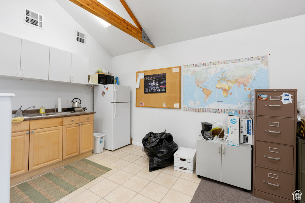 Kitchen with light tile flooring, white refrigerator, vaulted ceiling with beams, light brown cabinetry, and sink