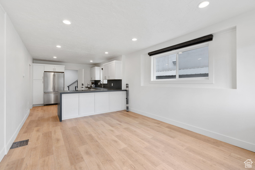 Kitchen with stainless steel refrigerator, kitchen peninsula, light hardwood / wood-style floors, and white cabinetry
