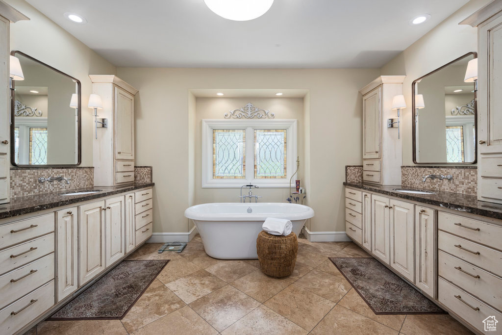Bathroom featuring backsplash, double sink vanity, a bathing tub, and tile flooring