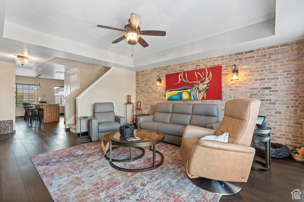 Living room with brick wall, ceiling fan, dark hardwood / wood-style floors, and a tray ceiling